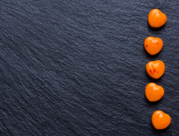 Píldoras en forma de corazón naranja o dulces en el fondo de pizarra negro grunge. Copiar espacio . —  Fotos de Stock