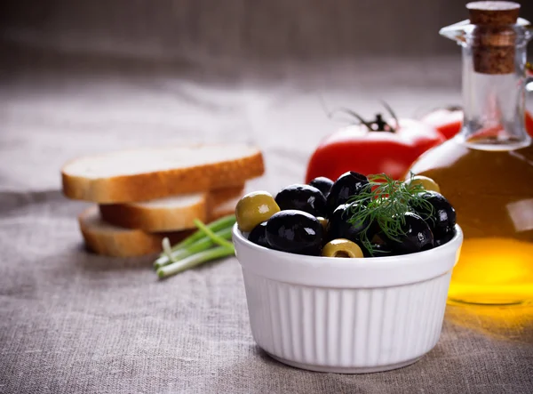 Olives in white bowl and small bottle of olive oil on jute fabric — Stock Photo, Image