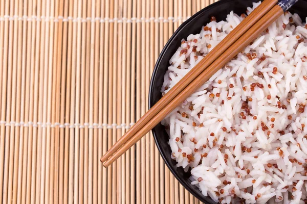 Ciotola di riso bianco e quinoa con bacchette su tappetino di bambù . — Foto Stock