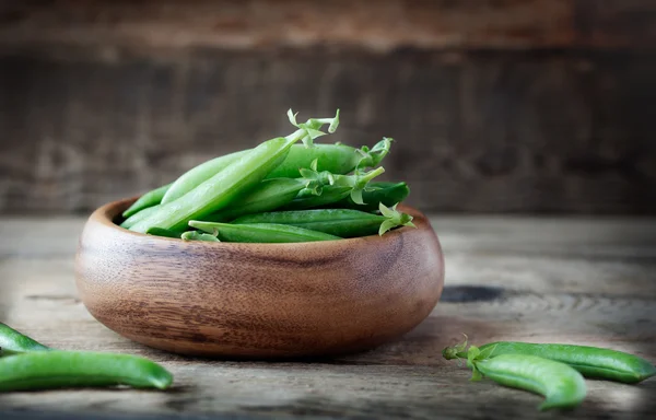 Green peas in wooden bowl — Stock Photo, Image