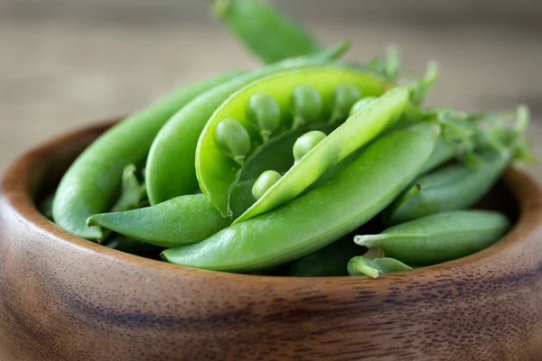 Green peas in wooden bowl — Stock Photo, Image