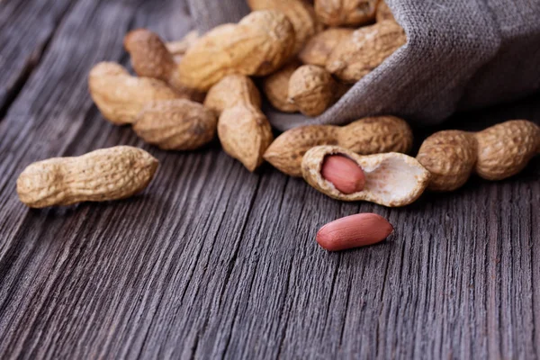 Pinda's in een miniatuur jute zak op houten oppervlak — Stockfoto