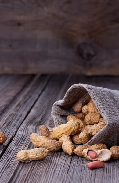 Pinda's in een miniatuur jute zak op houten oppervlak — Stockfoto