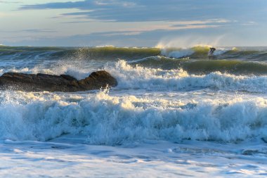 Fransa 'nın güneşli bir gününde okyanus dalgalarında sörf yapan bir sörfçü.