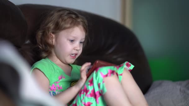 Flicka vilar på soffan med hjälp av smartphone, spela spel, titta på tecknad film, ha kul på internet. — Stockvideo