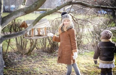 Blurred View of girls feeding birds in spring, birdhouse . High quality photo clipart