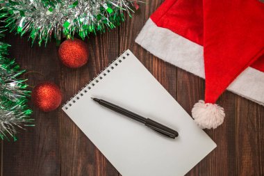 Not defteri, siyah kalem ve Noel Baba şapkası Noel topları ve çelenk ile ahşap bir masada. Düz Yatay