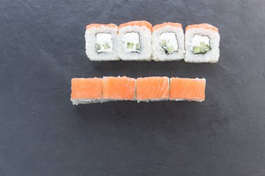 Siyah taş bir tahtanın üzerinde somonla yuvarlanıyor. Yemeği servis et. Pirinç, balık, avokado..