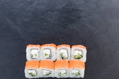 Siyah taş bir tahtanın üzerinde somonla yuvarlanıyor. Yemeği servis et. Pirinç, balık, avokado..