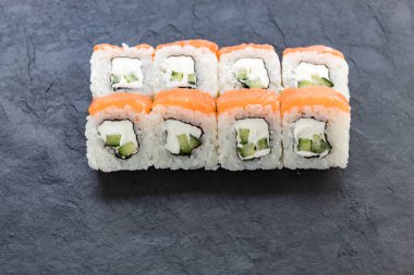 Siyah taş bir tahtanın üzerinde somonla yuvarlanıyor. Yemeği servis et. Pirinç, balık, avokado..