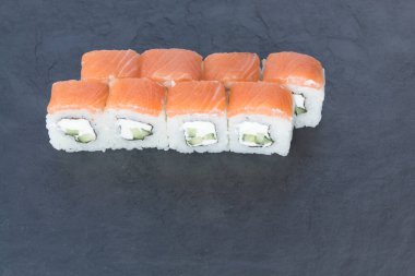 Siyah taş bir tahtanın üzerinde somonla yuvarlanıyor. Yemeği servis et. Pirinç, balık, avokado..