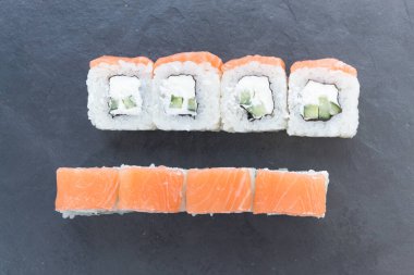 Siyah taş bir tahtanın üzerinde somonla yuvarlanıyor. Yemeği servis et. Pirinç, balık, avokado..