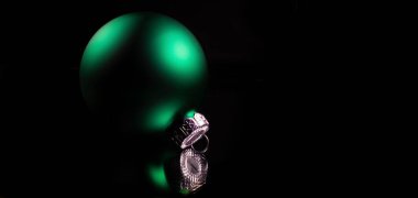 Karanlık bir yüzeye yansıyan siyah arkaplanı olan yeşil Noel süsü..