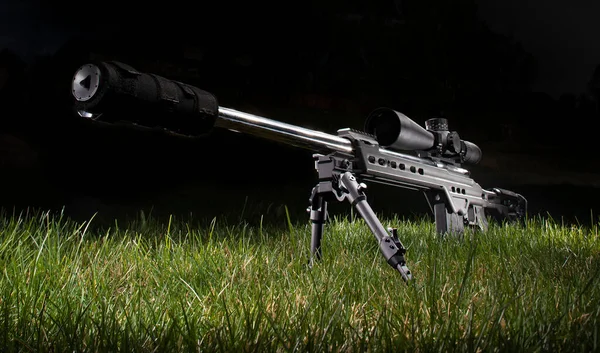 Sniper rifle with silencer and scope in the dark on the grass