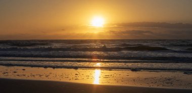 Güney Carolina Pawleys Adası 'ndaki Atlantik Okyanusu kıyısına vuran parlak turuncu güneş..
