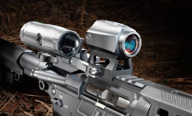 AR-15 kırmızı bir nokta optik ve büyüteç monte edilmiş, ama karanlık bir orman zemininde, çam iğneleriyle kaplanmış bir şekilde sallandı..