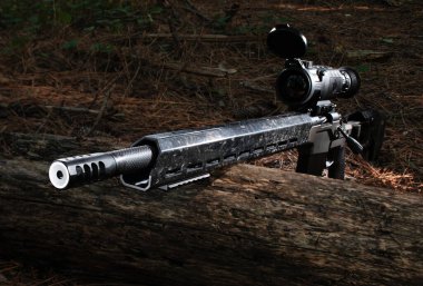 Ön tarafında monte edilmiş yüzeyleri olan tüfeği bir kütüğün üzerinde duruyor ve karanlıkta görmeye hazır, tabancaya takılı termal gece görüşü ile..