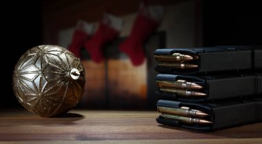 Tam kapasiteli AR-15 şarjörleri ve ahşap bir masanın üzerinde kırmızı çoraplı şöminenin arkasında yanan bir şömine ile altın bir Noel süsü..