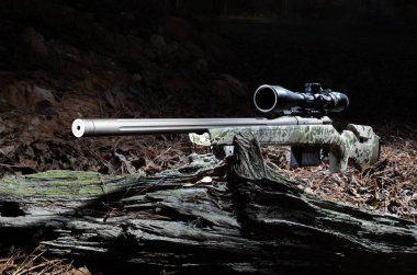 Tüfek, gece çürüyen bir kütüğün üzerine yerleştirilmiş kamuflaj malzemesi ve tüfek dürbünü ile avlanmak için bir sürgüdür..