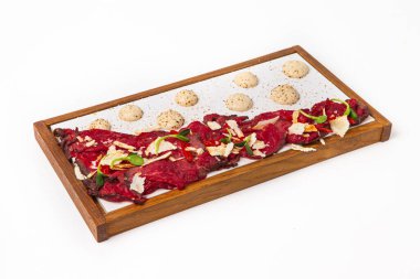 Parmesan, acı biber ve lahanayla dilimlenmiş sığır carpaccio, ahşap tepside sos damlalarıyla sunulur.