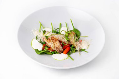 Taze ıspanaklı ızgara balık filetosu, bebek havuç, yeşil bezelye ve beyaz tabakta lezzetli bir sos.