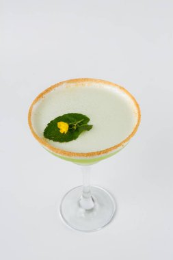 Açık yeşil bir kokteyl garnitürlü bir martini bardağında şeker kenarlı, temiz beyaz bir arka planda izole edilmiş.
