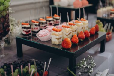Siyah ekran standında çeşitli tatlılar. Tatlı ikram için küçük porsiyon kekler, kremalar ve taze çilekler.