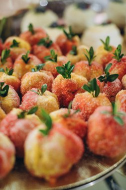 Renkli, tatlı, geleneksel İtalyan şeftali şekilli pastalar, pesche dolci olarak bilinir, şeker ve yeşil yapraklarla servis tabağında