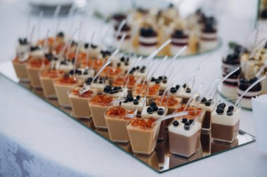 Aynalı bir tepside sunulan çikolatalı mus, krema ve meyve jölesi de dahil olmak üzere küçük plastik bardaklarda tatlı tatlılar.