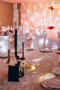 Zarif bir ziyafet masası, modern mum tutucuları, taze çiçekler ve altın tabaklar, özel bir kutlama için hazır.