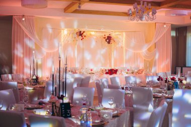 Etkinlik salonu, süslü masalar, çiçekli süsler ve sıcak ışıklandırmanın yer aldığı bir şenlik için hazırlandı.