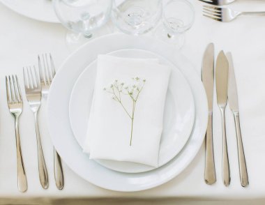 Beyaz tabaklar, peçete, çatal bıçak takımı ve hassas bir bebek nefesi etkinlikler için temiz, zarif bir masa süsü oluşturuyor.