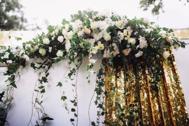 Beyaz ve pembe güllerden oluşan güzel bir çiçek çelengi, yeşil sarmaşık ve pırıl pırıl altın arkaplan içeren zarif bir düğün kemeri süslemesi.