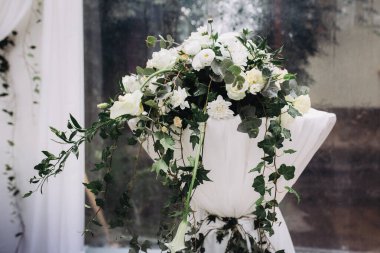 Beyaz taze çiçekler ve yemyeşil sarmaşık uzun bir masayı süslüyor, şenlikli bir etkinlik için zarif bir ortam oluşturuyor.