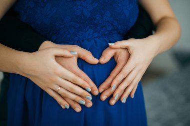 Hamile bir kadının karnında, sevgi, yeni hayat ve aile bağını sembolize eden bir kalp şekli oluşturan ebeveynler bekliyor.