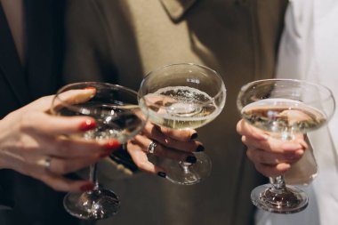 Şampanya kadehi tutan üç el köpüklü şarapla dolu, bir kutlama ya da sosyal etkinlikte kadeh kaldıran.