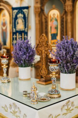 Ortodoks kilisesinde vaftiz töreni hazırlıkları, kutsal kaplar, yanan mumlar, lavanta ve ahşap bir haç.