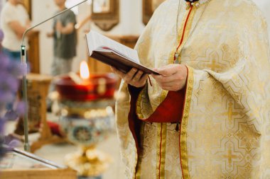Geleneksel cüppeli papaz kutsal bir kitap tutuyor, kilisede dini bir tören yapıyor, yanan bir mumla.