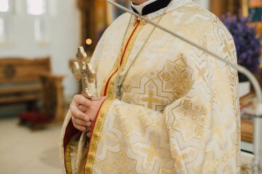 Kilisenin içinde dini bir tören sırasında elinde altın haç tutan süslü cübbeli rahip, inanç ve ayini temsil ediyor.