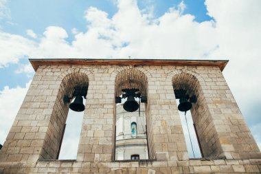 Üç büyük kemerli taş çan kulesi, tarihi bir kilise binasının bir parçası, güneşli mavi gökyüzüne karşı.