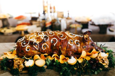 Taze sebzeler, cipsler ve süslemelerle süslü bir tabakta sunulan tam kavrulmuş süt domuzu ziyafet için hazır.