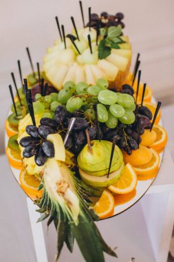 Üzüm, portakal, ananas, kavun ve armudu sağlıklı bir aperatif veya açık büfe olarak sunan çeşitli taze meyve tabakları.