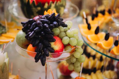Koyu üzümler, yeşil üzümler, elmalar ve açık büfe veya parti masasında armut içeren çeşitli taze meyve tabakları.