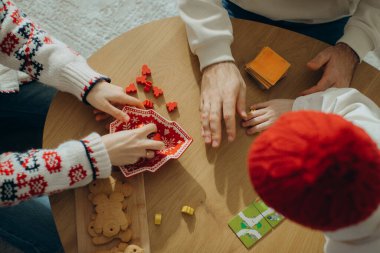 Aile üyeleri ahşap bir masanın etrafında toplanmış kırmızı parçalar ve zencefilli kurabiyelerle bir masa oyunu oynuyorlar.