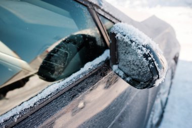Aracın yan aynası ve penceresi taze kar ve buzla kaplı. Park halindeki bir arabada kış havası koşullarını gösteriyor.