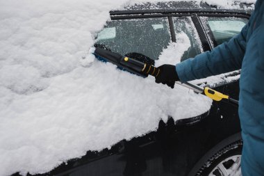 Soğuk kış sabahında, kar fırçasıyla ağır kar ve buzu arabanın penceresinden ve çatısından temizlerken güvenli sürüş imkanı sağlamak için.