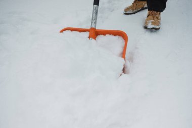 Kış kar yağdıktan sonra yoğun karı temizlemek için turuncu kürek kullanan işçi botları giyip gerekli bakımı yapıyor.