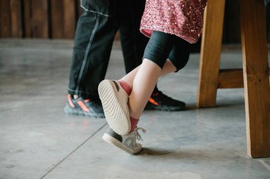 Çocuğun ayağı ebeveynin ayakkabısında dinleniyor. Nesiller arasında aile bağlarını, güveni ve artan bağlantıları gösteren neşeli bir an.