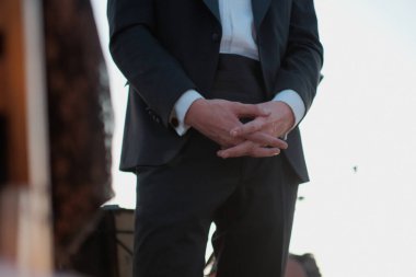 Damat, işadamı, ya da resmi olarak ayakta duran bir konuk, elleri sımsıkı bağlı, özel bir etkinlikte ya da törende smokin giyiyor.