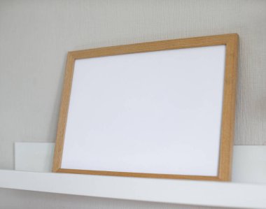 Boş ahşap çerçeve beyaz bir raf üzerinde bir ışık duvarına yaslanmış, içerik için boş alan sunuyor